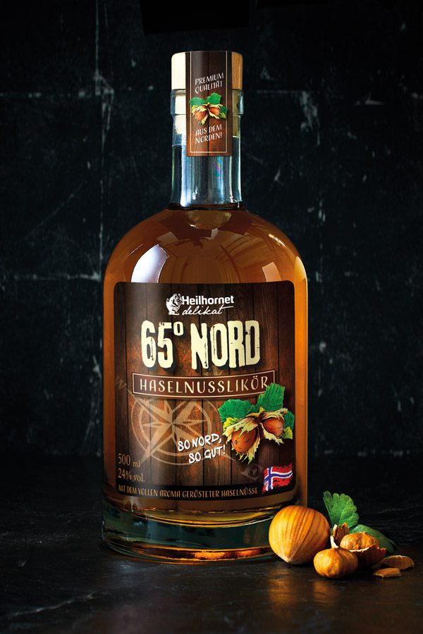 Heilhornet 65° Nord Haselnusslikör-Flasche mit Produktetikett und Haselnüssen auf dunkler Oberfläche. – Fishing Adventure GmbH