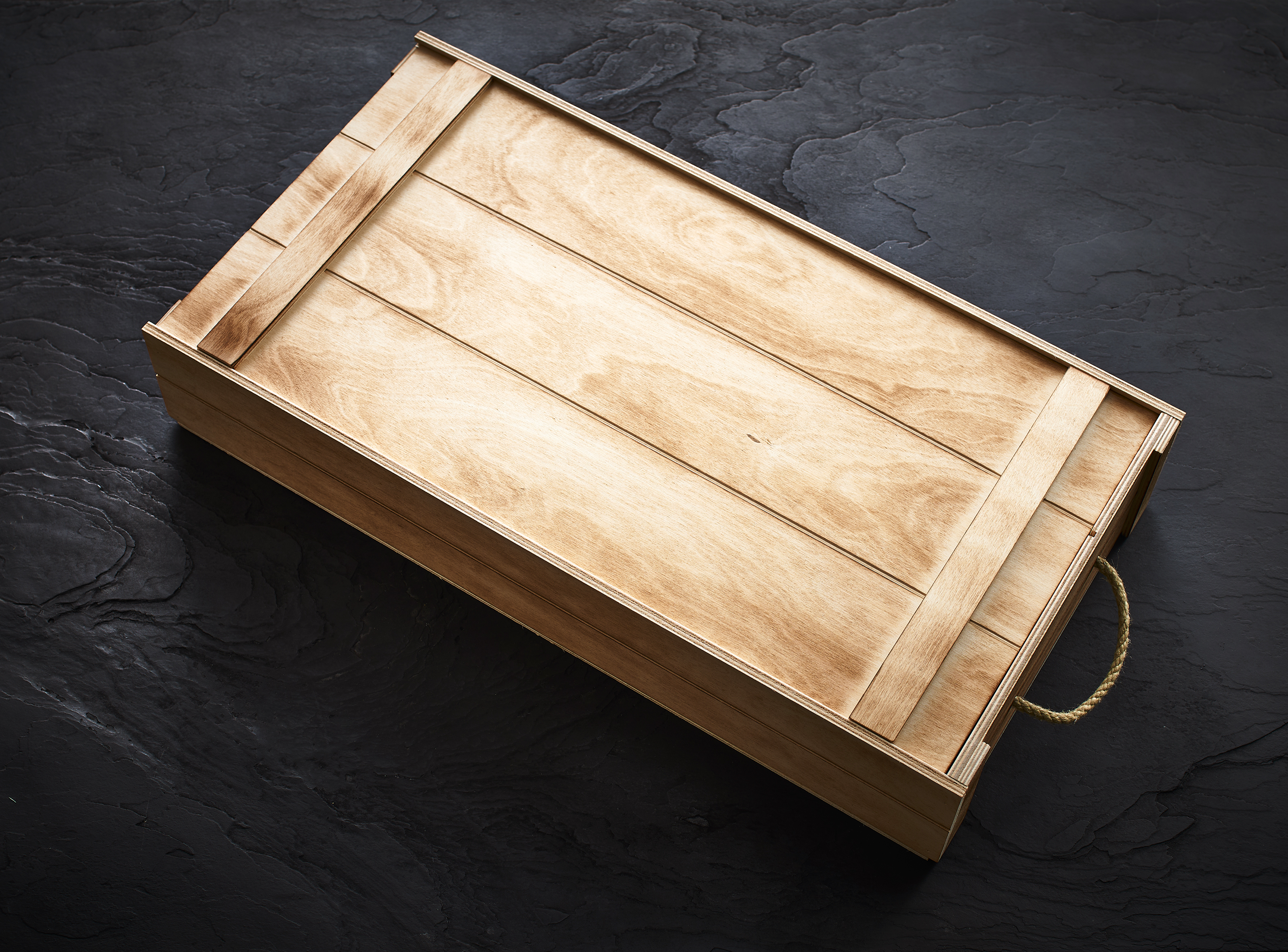 Aufbewahrungsbox aus Holz mit Seilgriff, zum Organisieren von Angelgeräten oder Outdoor-Ausrüstung auf einer dunklen Oberfläche. – Fishing Adventure GmbH
