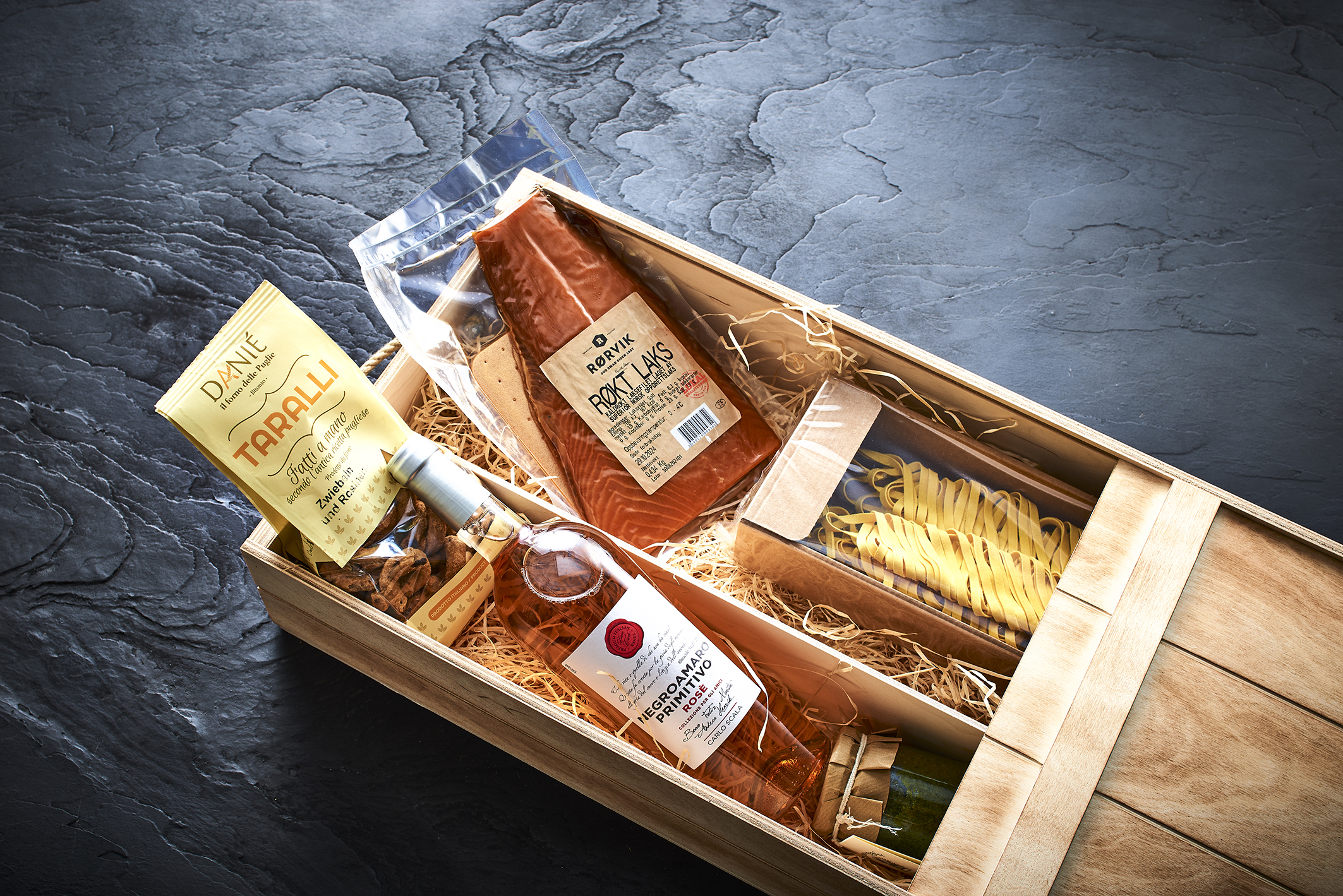 Geschenkkorb mit geräuchertem Lachs, Wein, Pasta und Taralli-Crackern, präsentiert in einer rustikalen Holzkiste. – Fishing Adventure GmbH