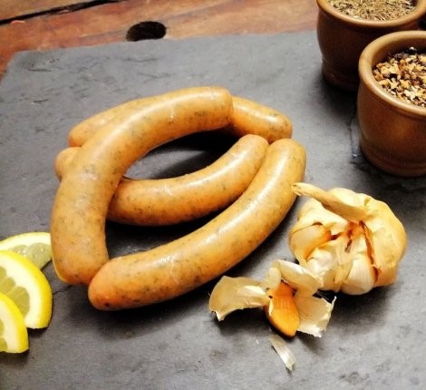 Nahaufnahme mehrerer Würstchen mit Zitronenscheiben und Knoblauchknolle auf einer dunklen Oberfläche mit Gewürzen in kleinen Behältern. – Fishing Adventure GmbH