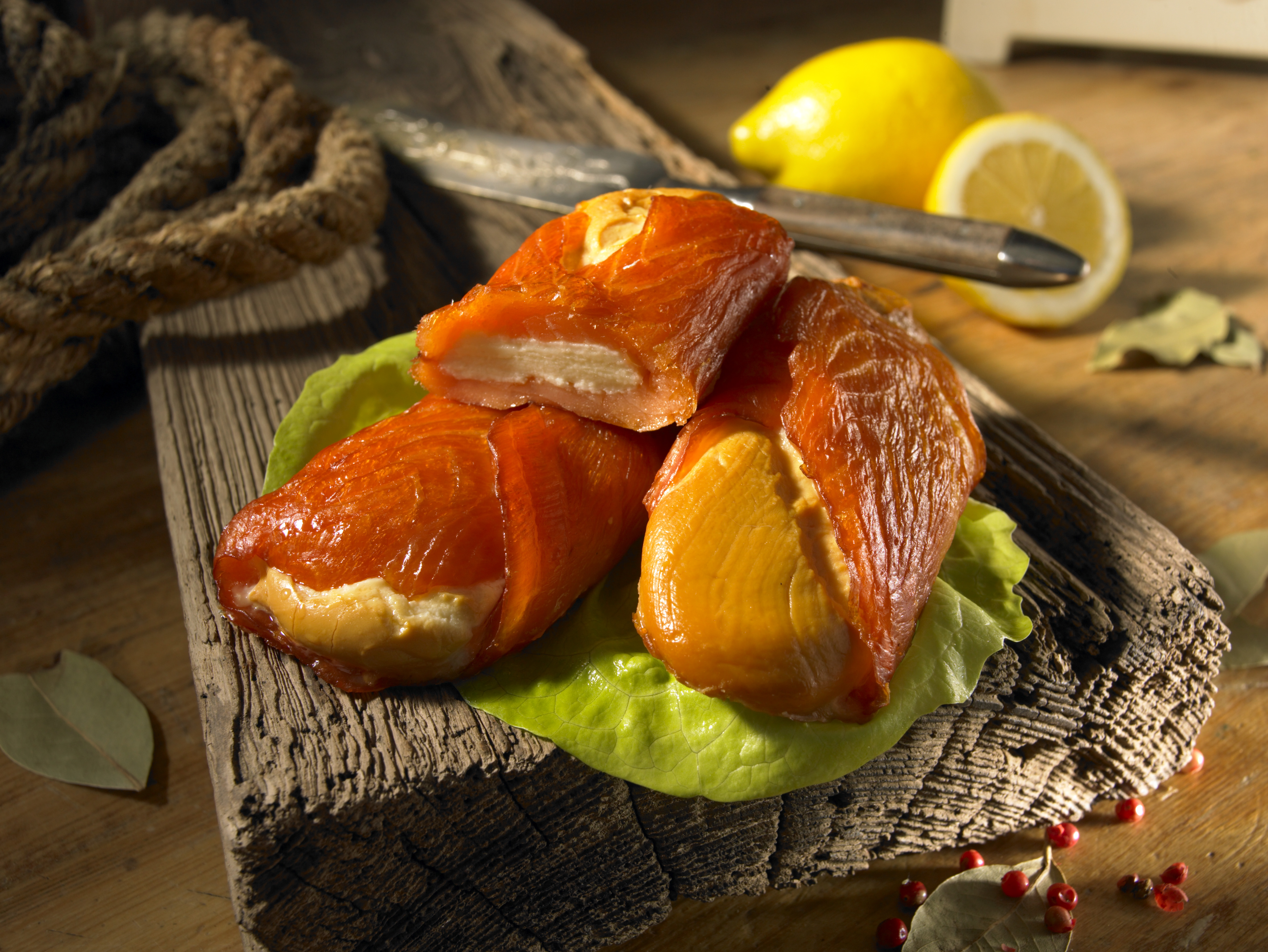 Vorspeisen mit geräuchertem Lachs auf Salatblättern mit Zitronen und einem Messer auf einem Holzbrett. – Fishing Adventure GmbH