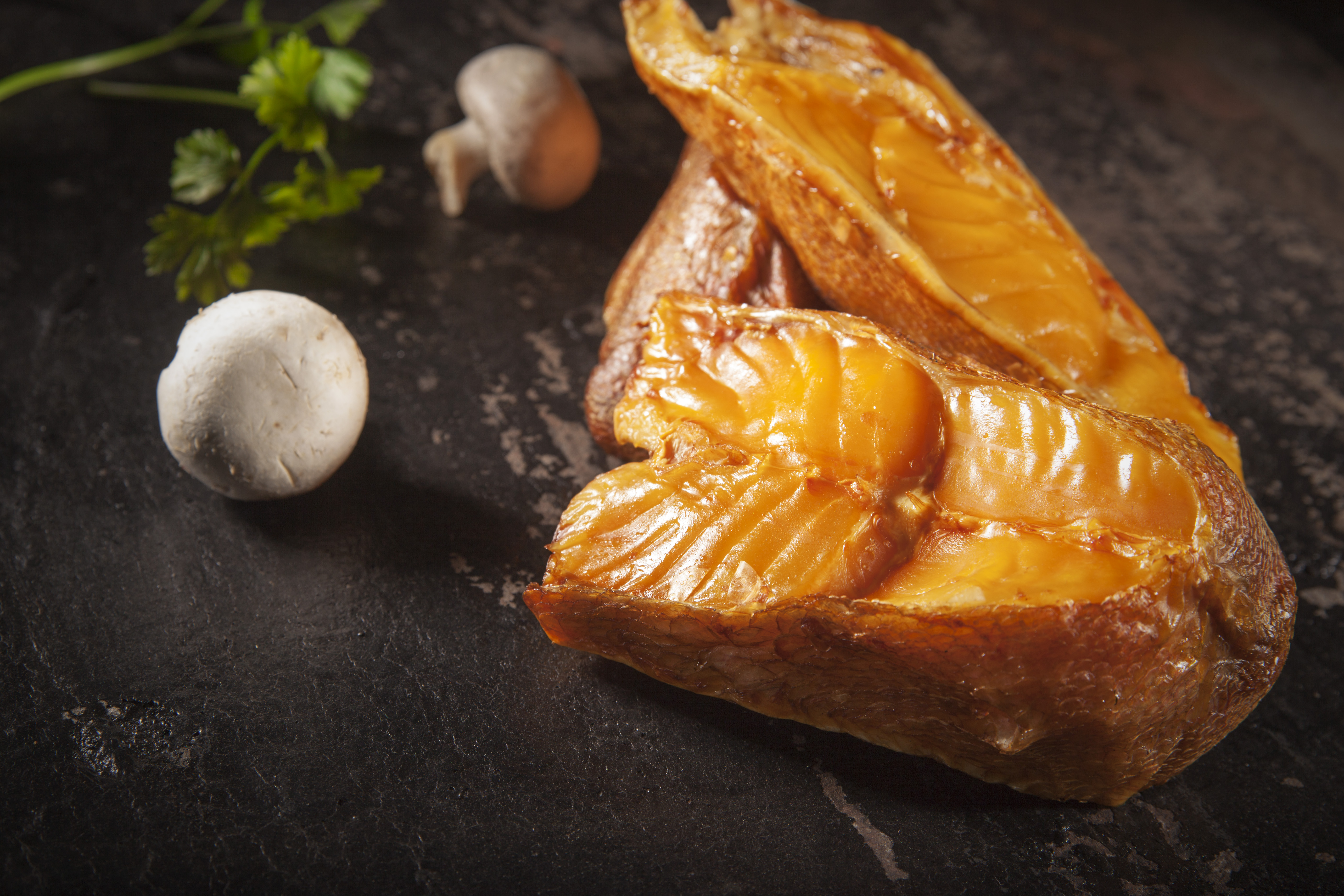 Nahaufnahme von geräucherten Lachsfilets mit Pilzen und Petersilie auf dunklem Schieferhintergrund. – Fishing Adventure GmbH