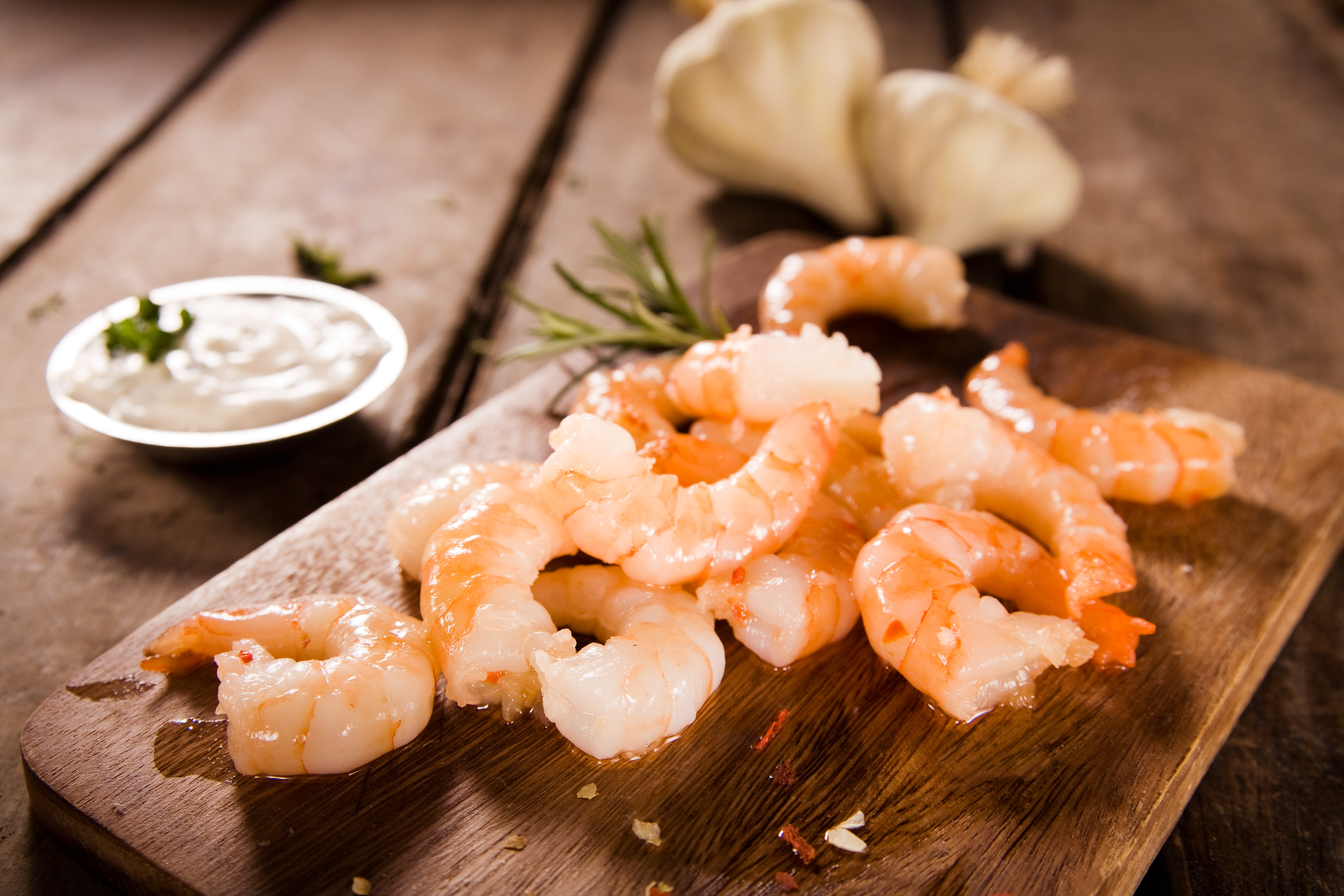 Gekochte Garnelen serviert auf einem Holzbrett mit cremiger Sauce und Knoblauchknollen im Hintergrund. – Fishing Adventure GmbH